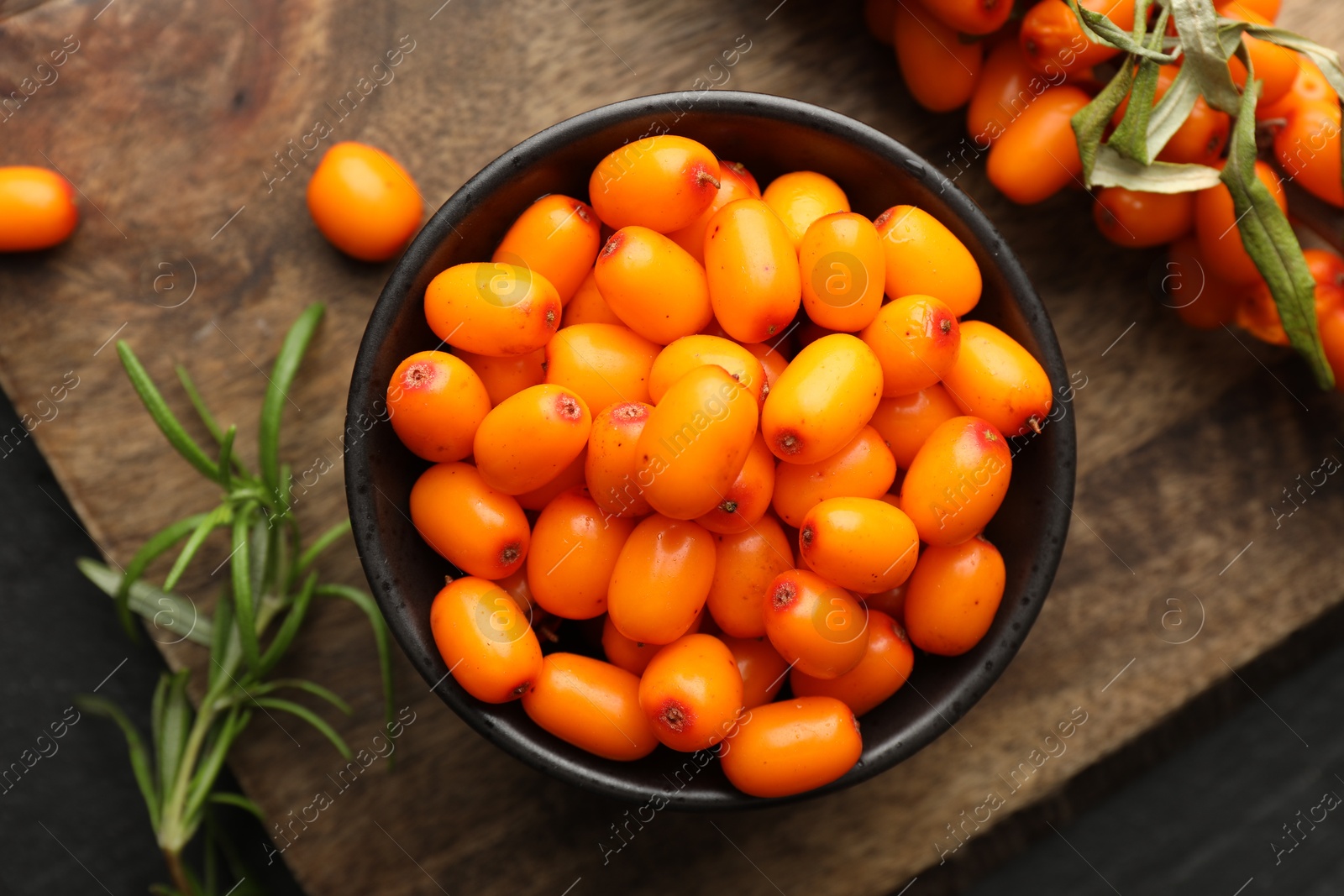 Photo of Fresh sea buckthorn berries with leaves in bowl on black table, top view