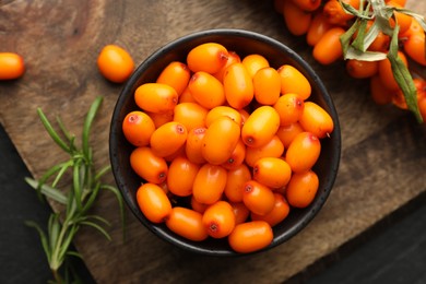 Photo of Fresh sea buckthorn berries with leaves in bowl on black table, top view