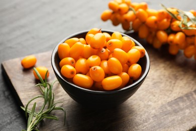 Photo of Fresh sea buckthorn berries with leaves in bowl on black table, closeup
