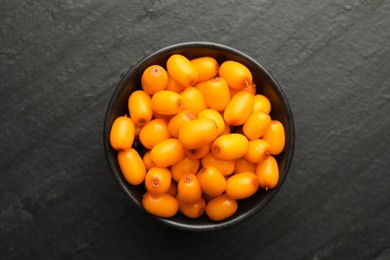 Photo of Fresh sea buckthorn berries in bowl on black table, top view