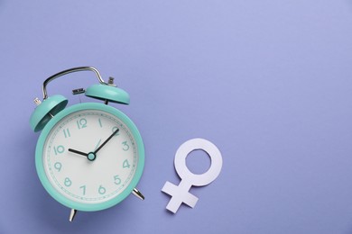 Photo of Menopause. Female gender symbol and alarm clock on violet background, flat lay. Space for text