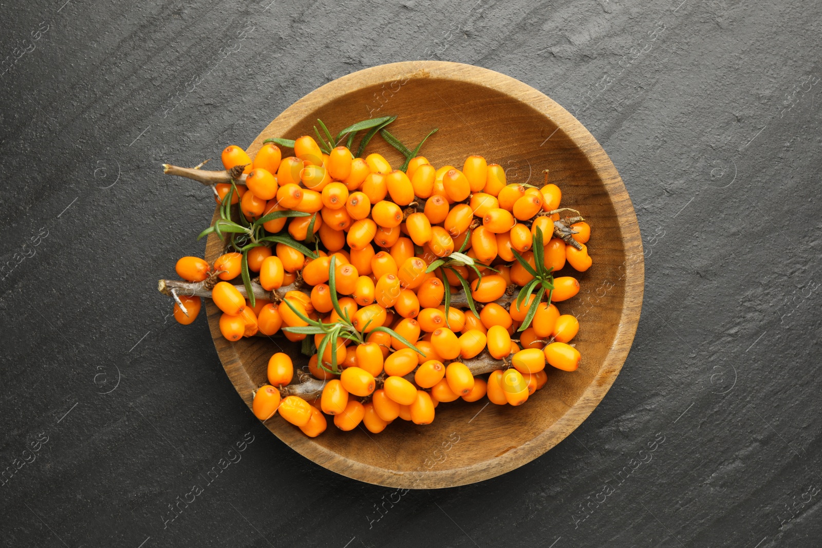 Fresh sea buckthorn berries with leaves in bowl on black table, top view Photo of Fresh sea buckthorn berries with leaves in bowl on black table, top view