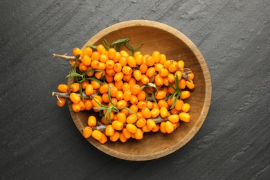 Photo of Fresh sea buckthorn berries with leaves in bowl on black table, top view