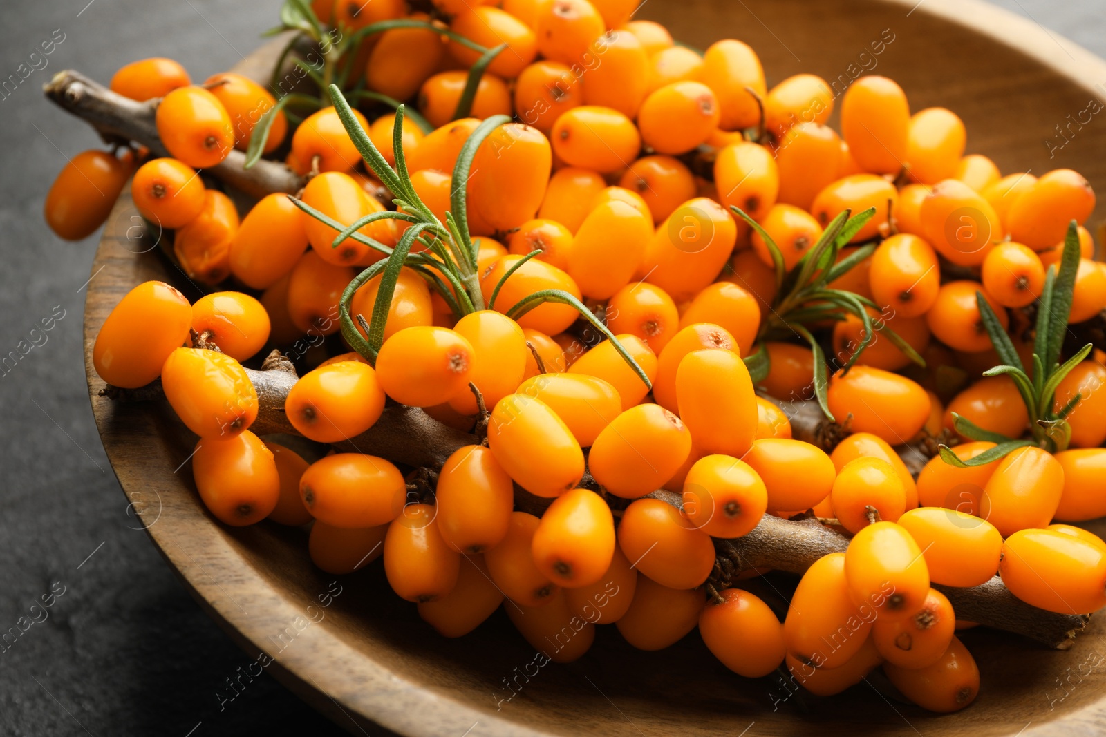 Photo of Fresh sea buckthorn berries with leaves in bowl on black table, closeup