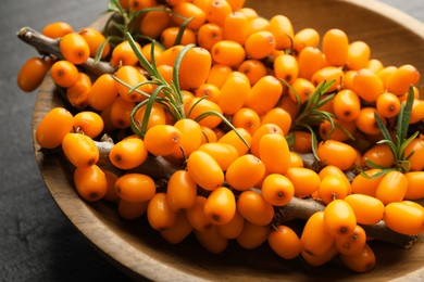Photo of Fresh sea buckthorn berries with leaves in bowl on black table, closeup