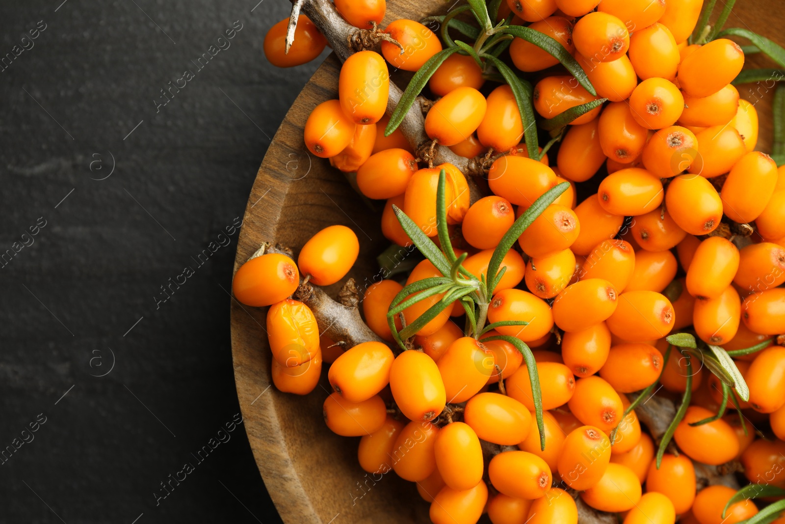 Photo of Fresh sea buckthorn berries with leaves in bowl on black table, top view