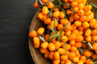 Photo of Fresh sea buckthorn berries with leaves in bowl on black table, top view