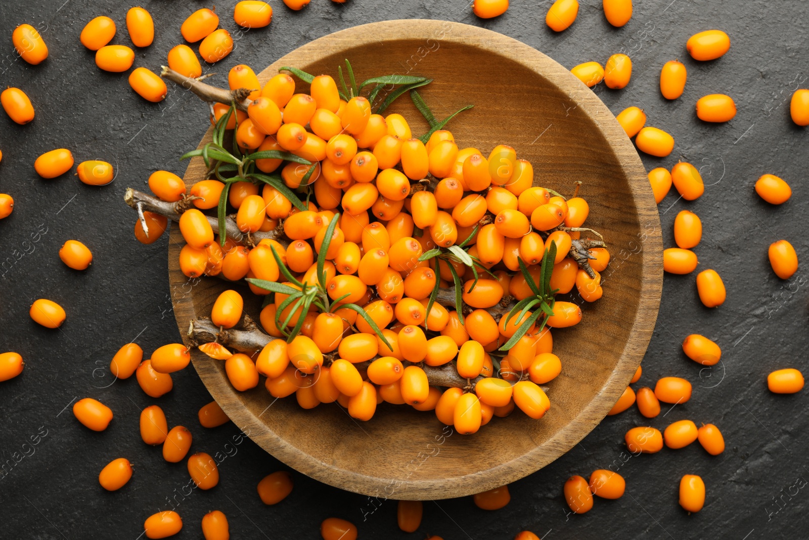 Photo of Fresh sea buckthorn berries with leaves in bowl on black table, flat lay