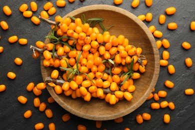 Photo of Fresh sea buckthorn berries with leaves in bowl on black table, flat lay
