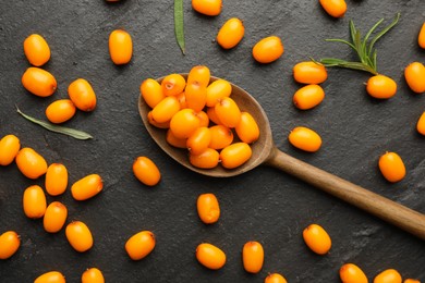 Photo of Fresh sea buckthorn berries, spoon and leaves in on black table, flat lay