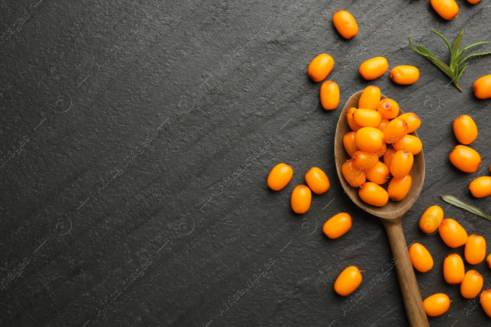 Photo of Fresh sea buckthorn berries, spoon and leaves in on black table, flat lay. Space for text