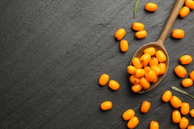 Photo of Fresh sea buckthorn berries, spoon and leaves in on black table, flat lay. Space for text