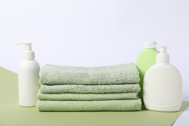 Photo of Stack of fresh terry towels and cosmetic products on color background