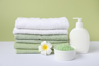 Photo of Stack of fresh terry towels, cosmetic products and plumeria flower on color background