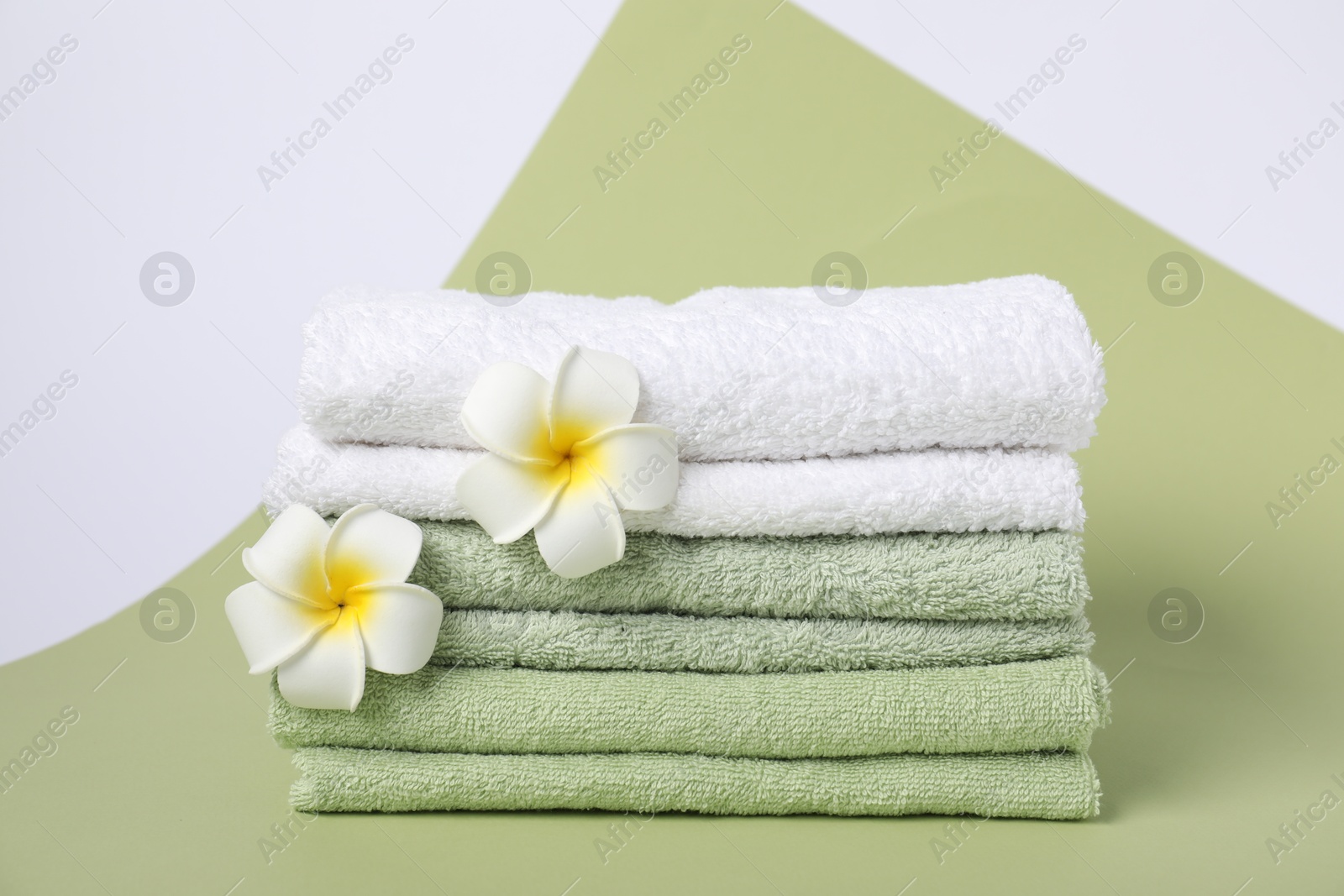 Photo of Stack of fresh terry towels and plumeria flowers on color background
