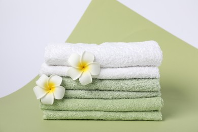 Photo of Stack of fresh terry towels and plumeria flowers on color background
