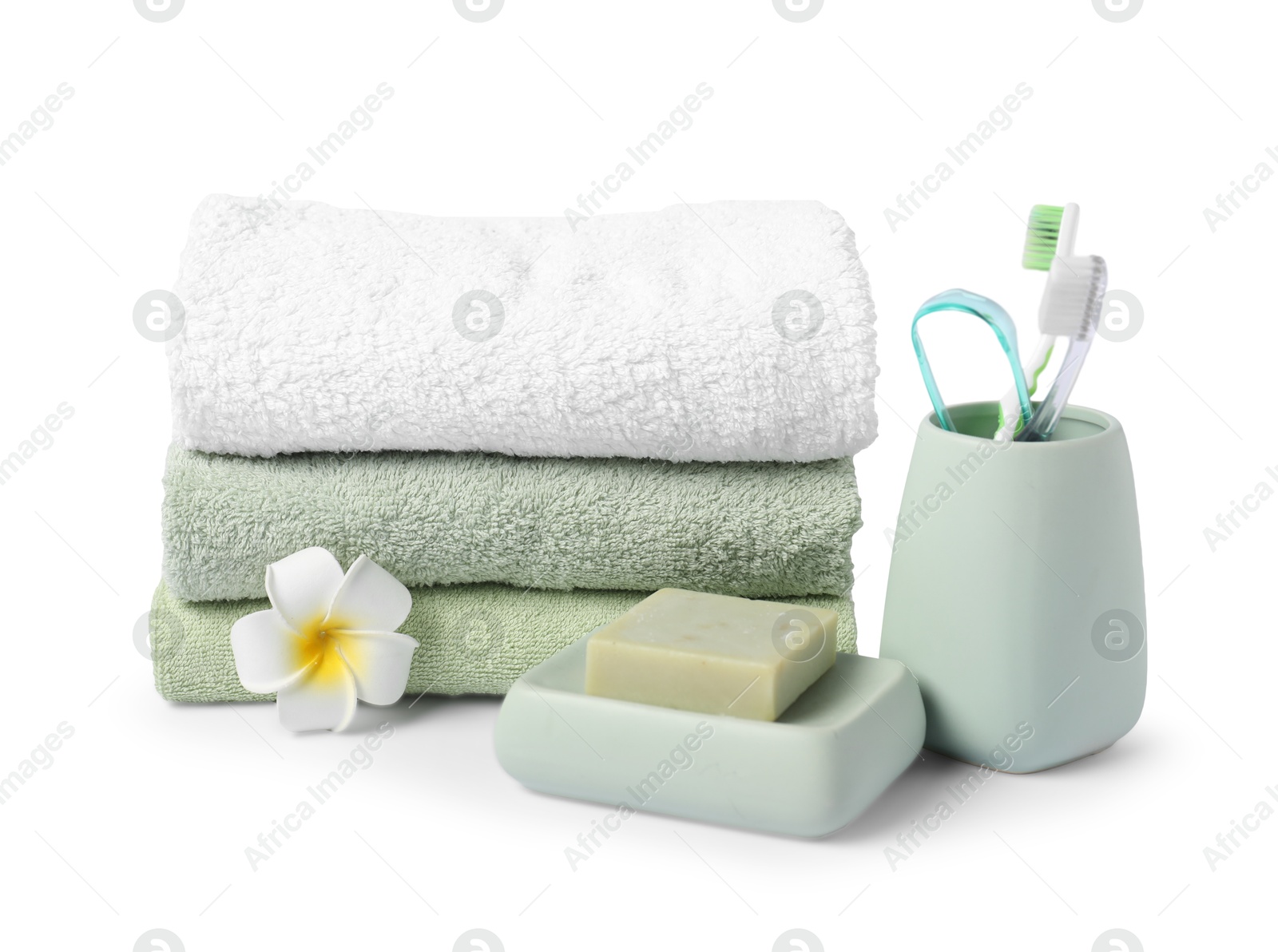 Photo of Stack of fresh terry towels, soap, toothbrushes and plumeria flower isolated on white