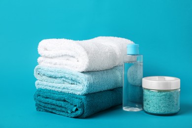 Photo of Stack of fresh terry towels and cosmetic products on light blue background