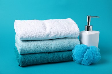 Photo of Stack of fresh terry towels, cosmetic product and sponge on light blue background