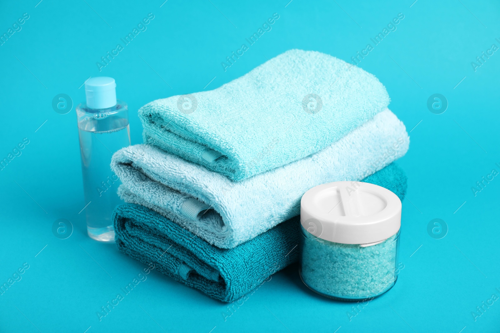 Photo of Stack of fresh terry towels and cosmetic products on light blue background