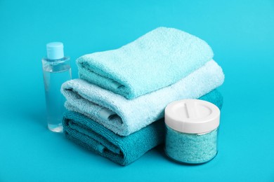 Photo of Stack of fresh terry towels and cosmetic products on light blue background