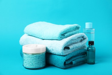 Photo of Stack of fresh terry towels and cosmetic products on light blue background