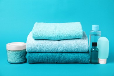Photo of Stack of fresh terry towels and cosmetic products on light blue background