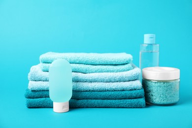 Photo of Stack of fresh terry towels and cosmetic products on light blue background