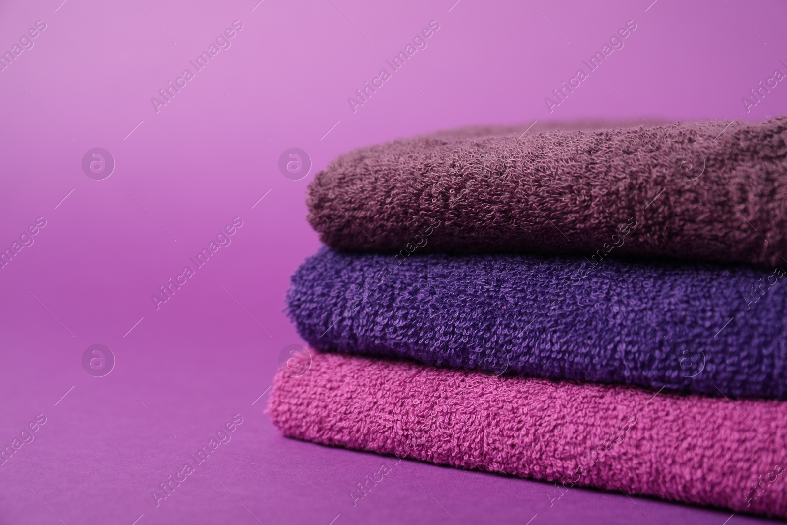 Photo of Stack of fresh terry towels on purple background, closeup. Space for text