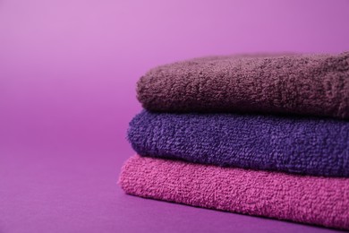 Photo of Stack of fresh terry towels on purple background, closeup. Space for text