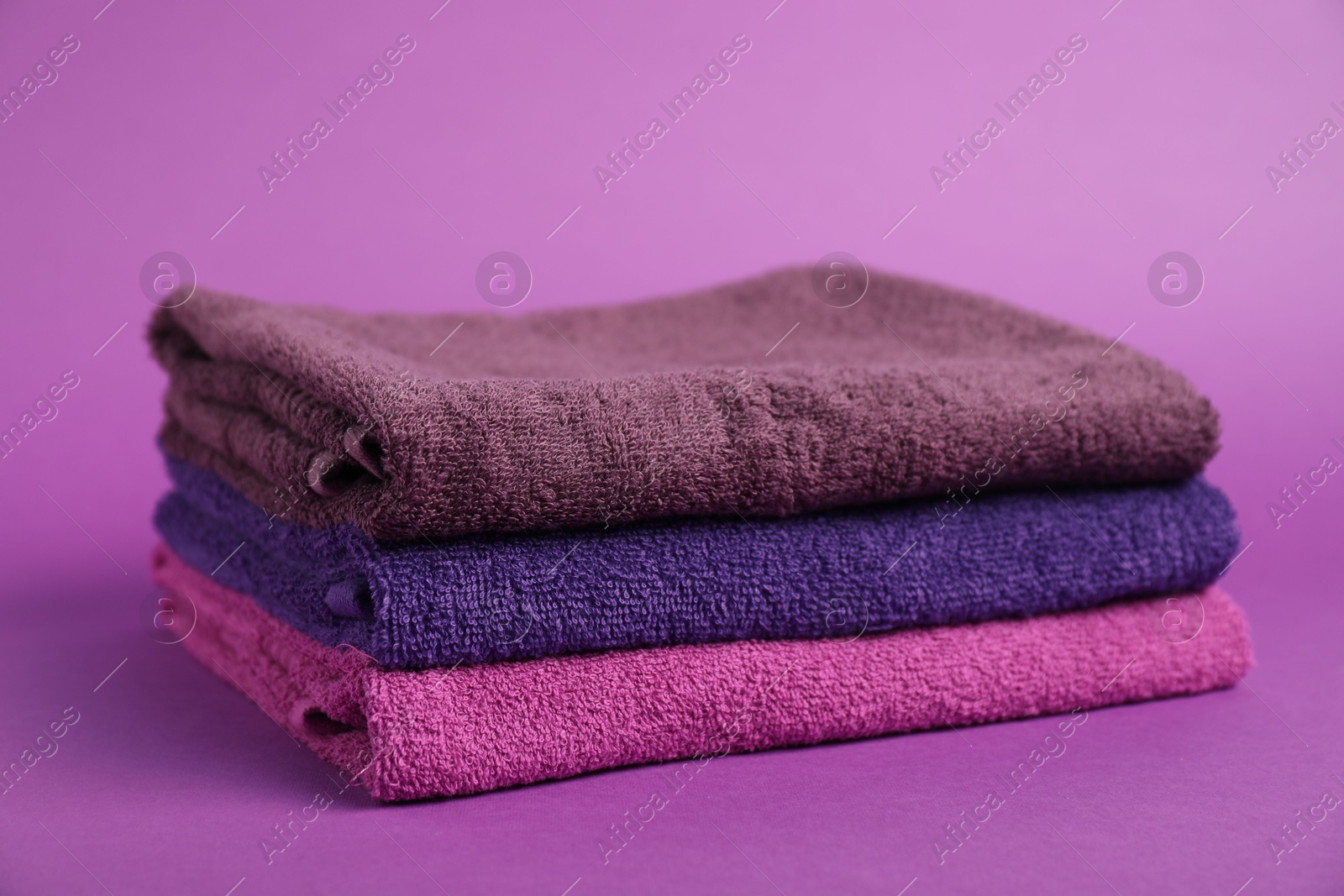 Photo of Stack of fresh terry towels on purple background, closeup