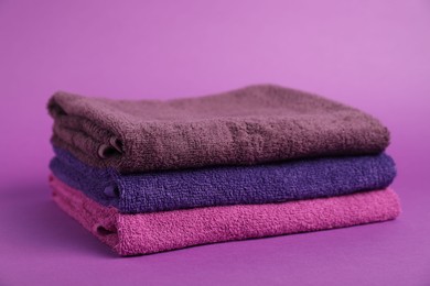 Photo of Stack of fresh terry towels on purple background, closeup