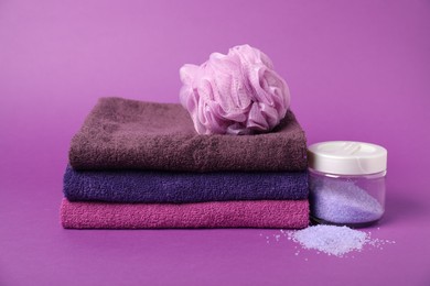 Photo of Stack of fresh terry towels, sponge and sea salt on purple background