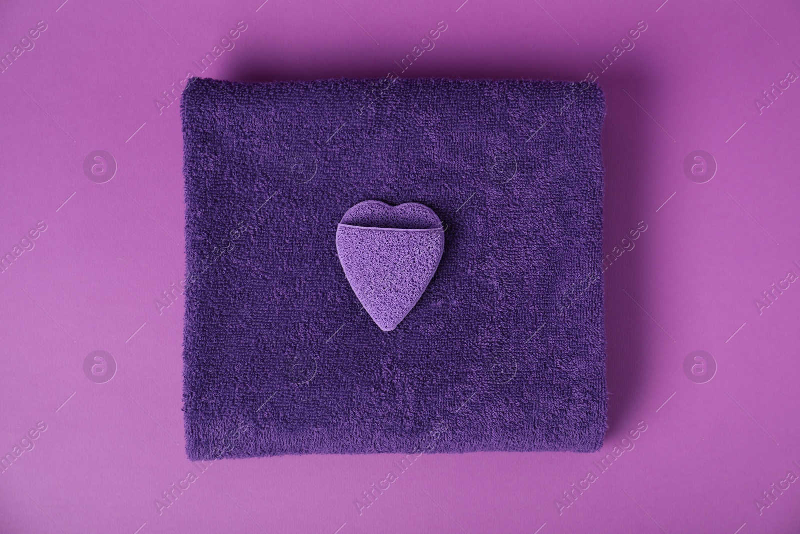 Photo of Fresh terry towel and sponge on purple background, top view