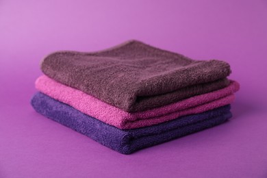 Photo of Stack of fresh terry towels on purple background, closeup
