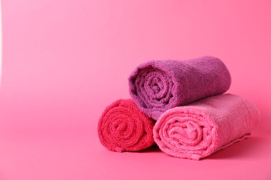 Photo of Rolled fresh terry towels on pink background, closeup. Space for text