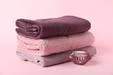 Photo of Stack of fresh terry towels and candle on pink background