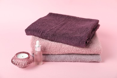 Photo of Stack of fresh terry towels, cosmetic product and candle on pink background