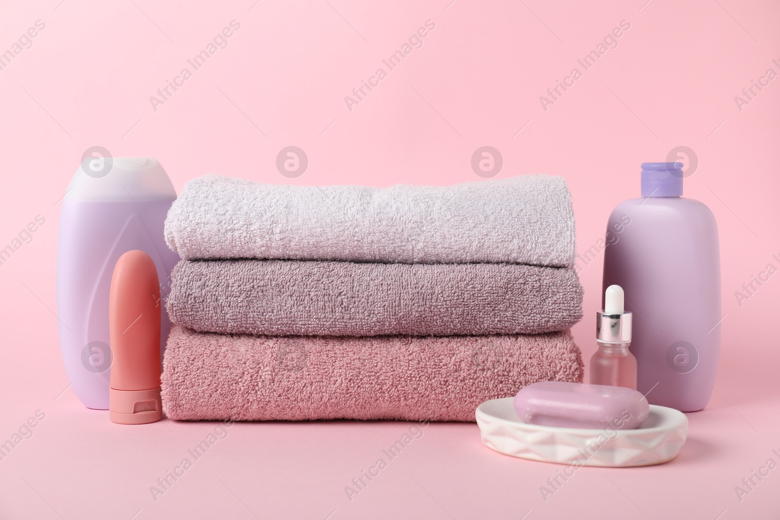 Photo of Stack of fresh terry towels and cosmetic products on pink background