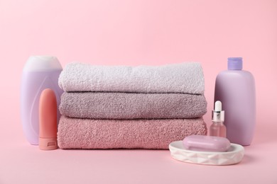Photo of Stack of fresh terry towels and cosmetic products on pink background