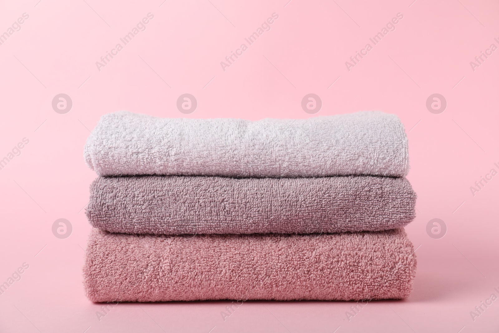 Stack of fresh terry towels on pink background Photo of Stack of fresh terry towels on pink background