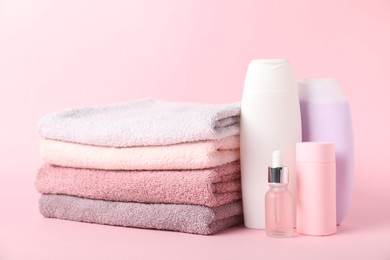 Photo of Stack of fresh terry towels and cosmetic products on pink background