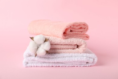 Photo of Stack of fresh terry towels and cotton flower on pink background