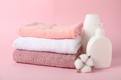 Photo of Stack of fresh terry towels, cosmetic products and cotton flower on pink background