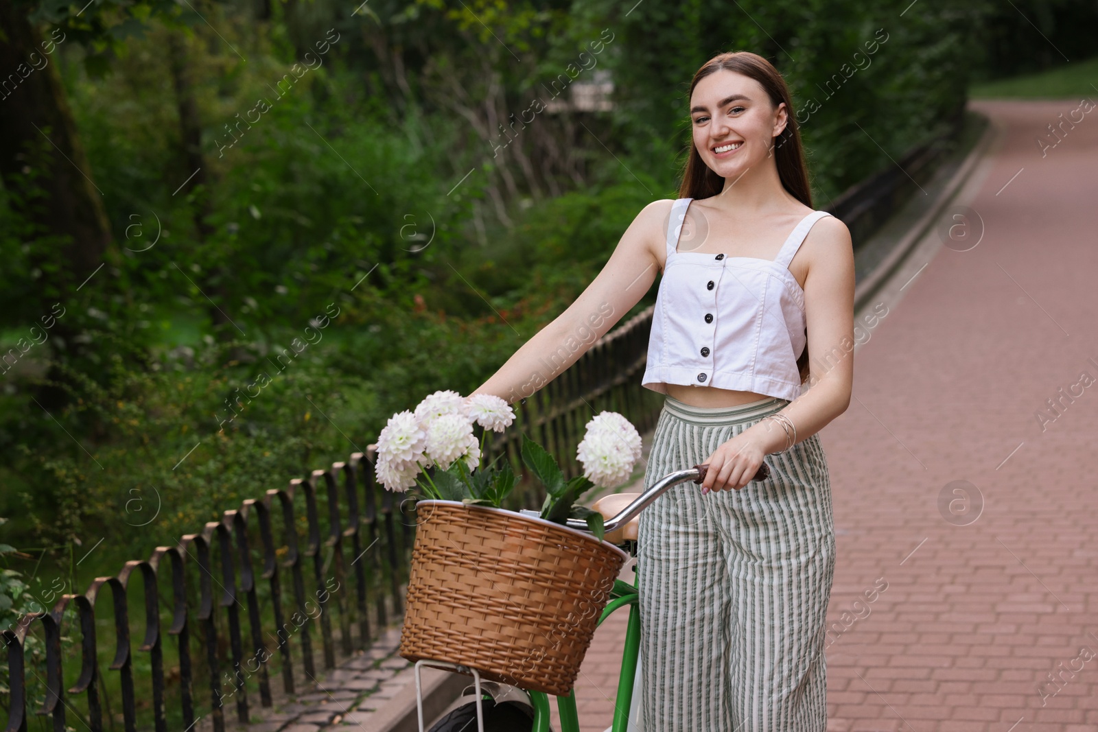 Photo of Woman walking her bicycle with flowers in basket outdoors. Space for text
