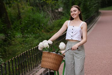 Photo of Woman walking her bicycle with flowers in basket outdoors. Space for text