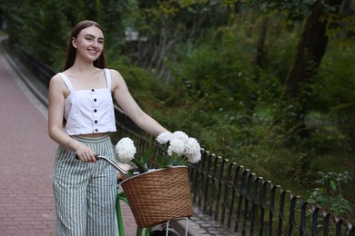 Photo of Woman walking her bicycle with flowers in basket outdoors. Space for text