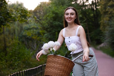 Photo of Woman walking her bicycle with flowers in basket outdoors. Space for text