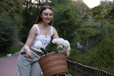 Photo of Woman walking her bicycle with flowers in basket outdoors. Space for text