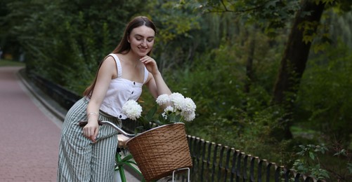 Photo of Woman walking her bicycle with flowers in basket outdoors. Space for text